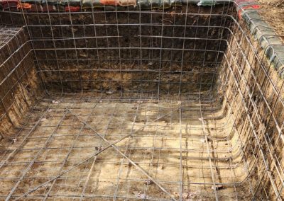 The construction process of a concrete pool, where only the hole has been dug, with the reinforcing wiring visible.