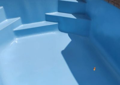 Cleaner concrete pool that is now renovated and blue.